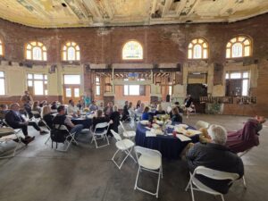 Attendees around round tables in an abandoned train station, listening to a speaker.